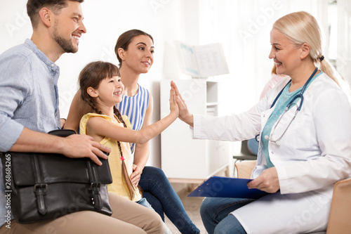 Cute child sitting with her parents and giving high five to doctor in hospital © New Africa