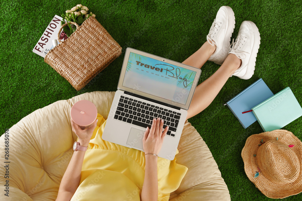 Fotografie Woman and laptop with travel blogger site on artificial grass, top view