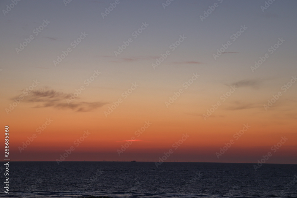Red and blue colors in the sky by the ocean with a ship at the horizon