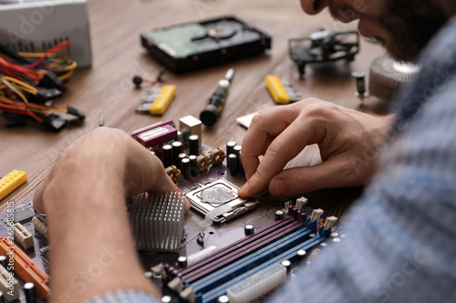Male technician repairing motherboard at table  closeup