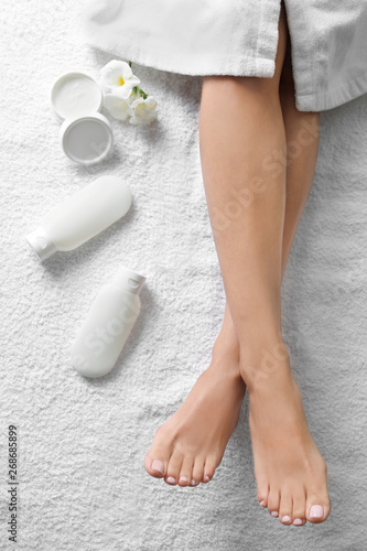Woman with beautiful feet and cosmetic products on white towel, top view. Spa treatment
