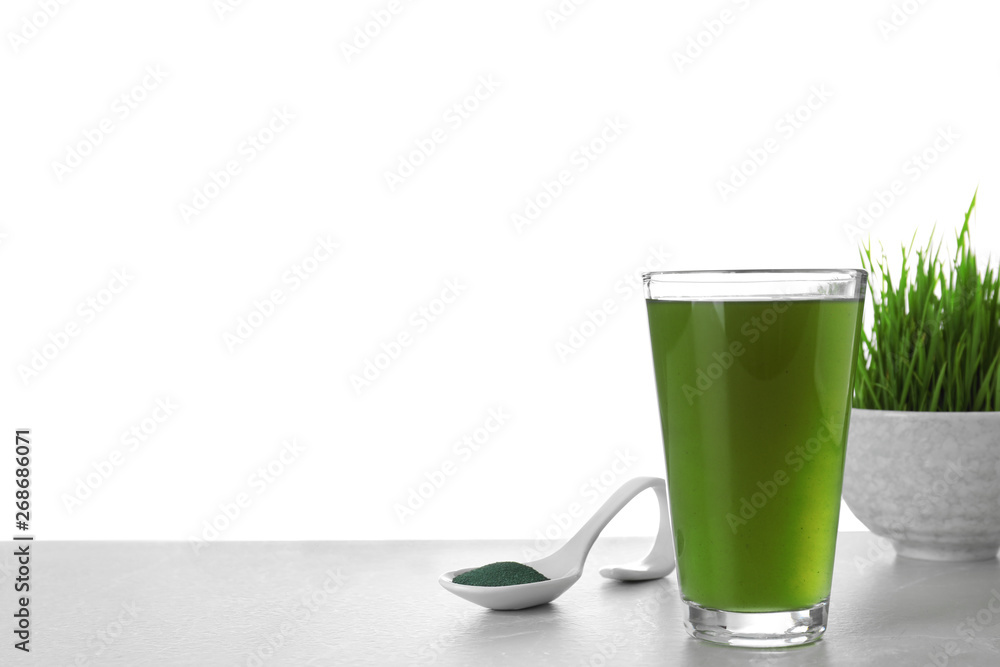Glass of spirulina drink and spoon with powder on table against white background. Space for text Glass of spirulina drink and spoon with powder on table against white background. Space for text