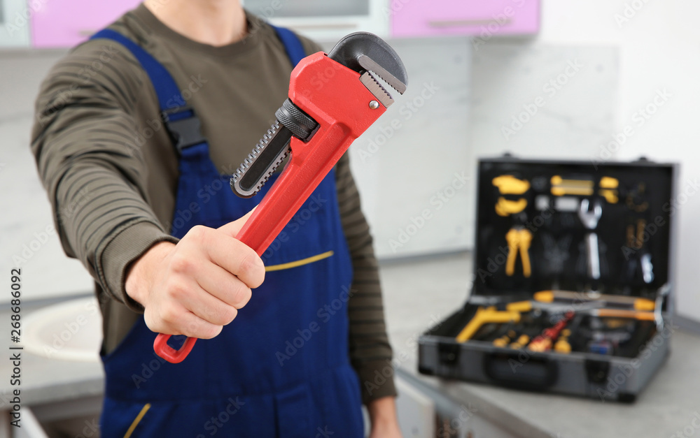 Male plumber holding pipe wrench in kitchen, closeup with space for text. Repair service Male plumber holding pipe wrench in kitchen, closeup with space for text. Repair service