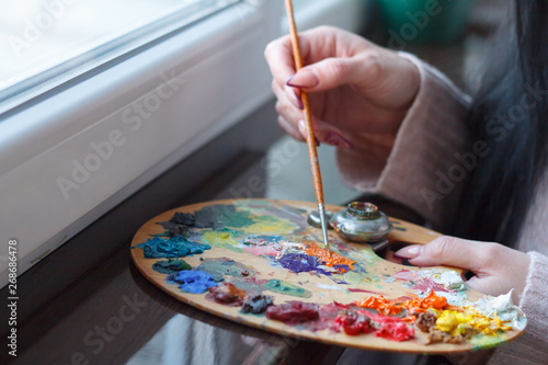 Close-up of female hands mixing paints on a palette with a spatula creating an oil painting