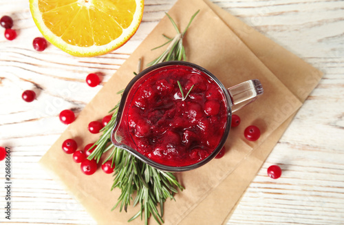 Tasty cranberry sauce in pitcher with rosemary on white wooden background, flat lay photo