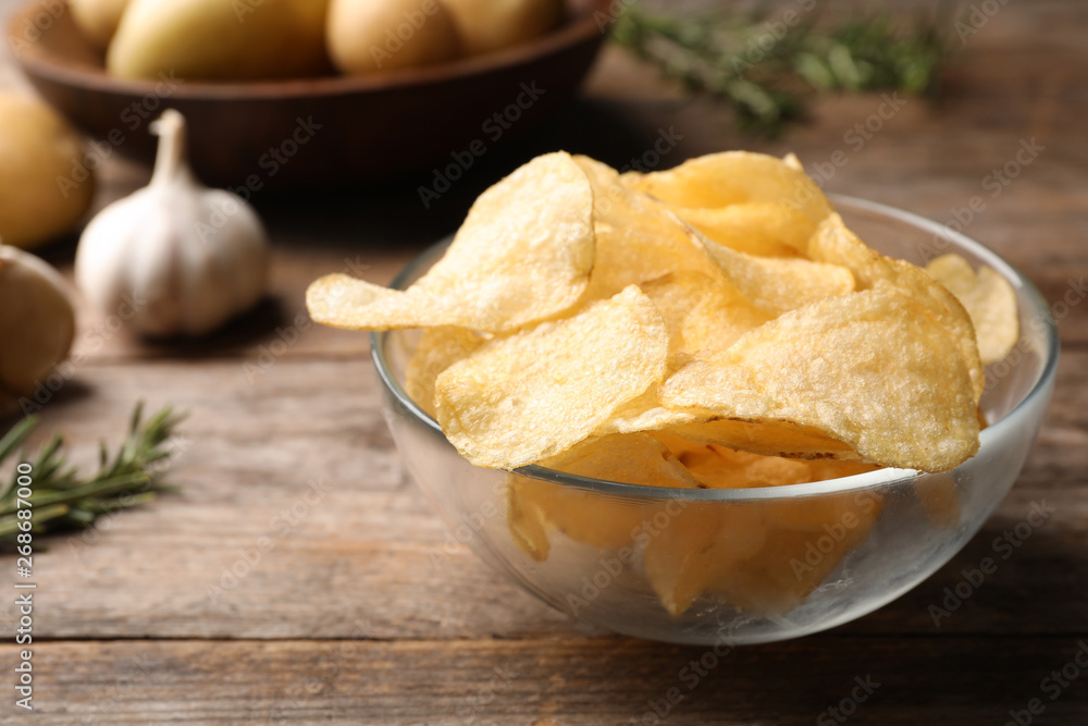 Bowl of crispy potato chips on wooden table. Space for text