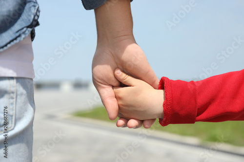 Little child holding hands with his father outdoors, closeup. Family weekend
