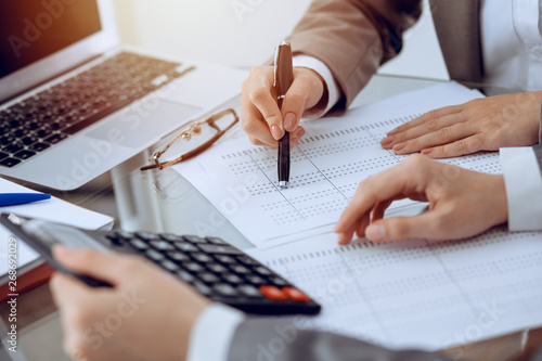 Two female accountants counting on calculator income for tax form completion hands close-up. Business and audit concept