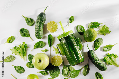 Fotografie, Obraz Green smoothie in cute glass jar shape of cactus with spinach and green fruits and vegetables on white table
