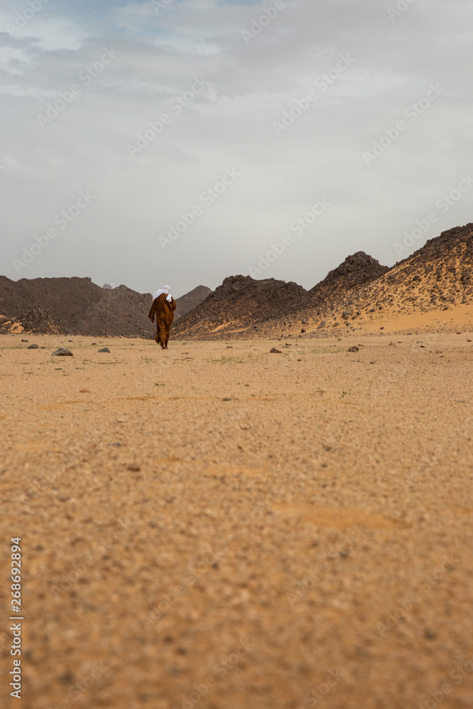 A Tuareg people walking in the Sahara Desert surrounded by mountains in Algeria A Tuareg people walking in the Sahara Desert surrounded by mountains in Algeria