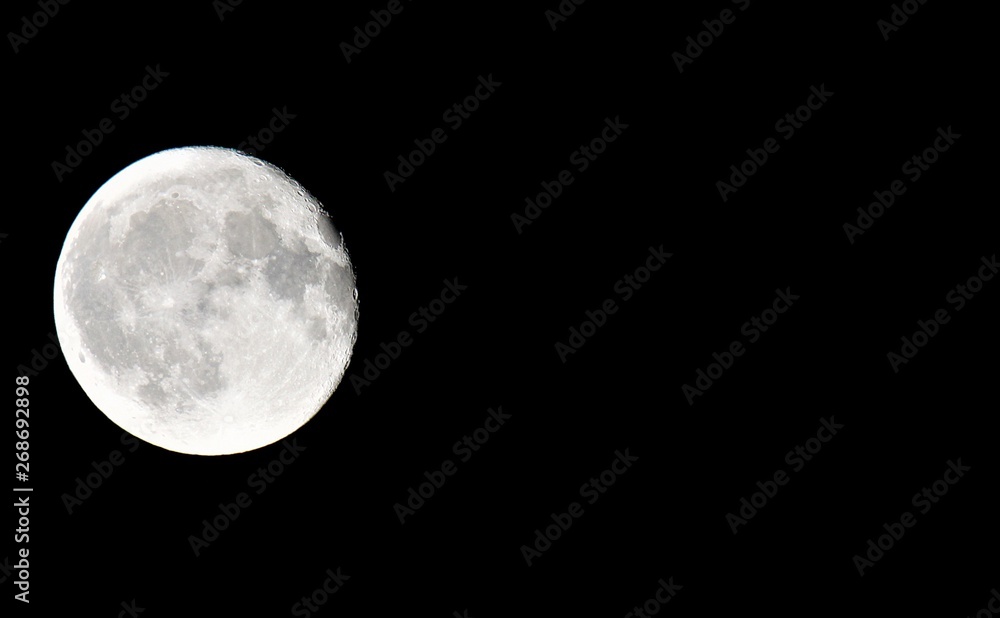 Fototapeta premium Close up of full moon with black background on left side of photo with copy space