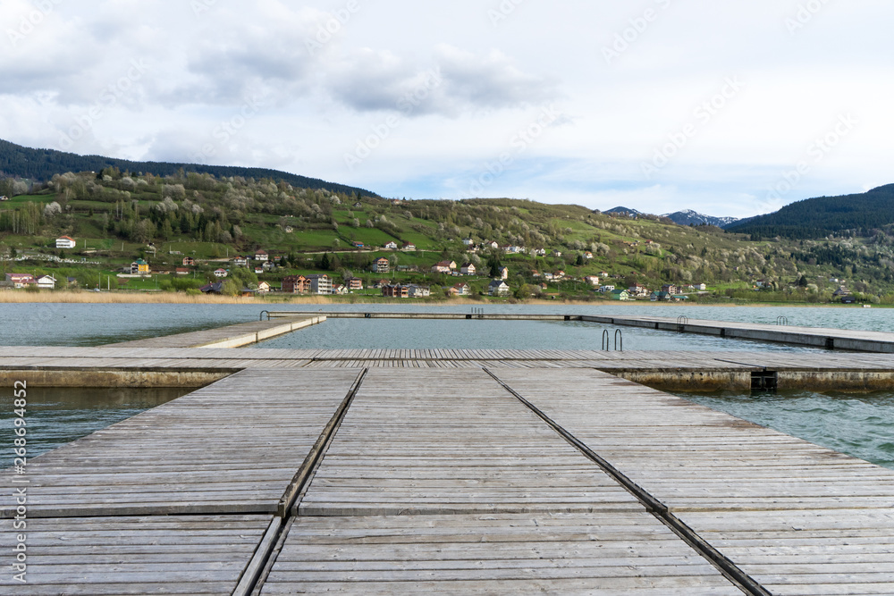 Idyllic view of the wooden pier in the lake with mountain scenery background. Plav lake montenegro