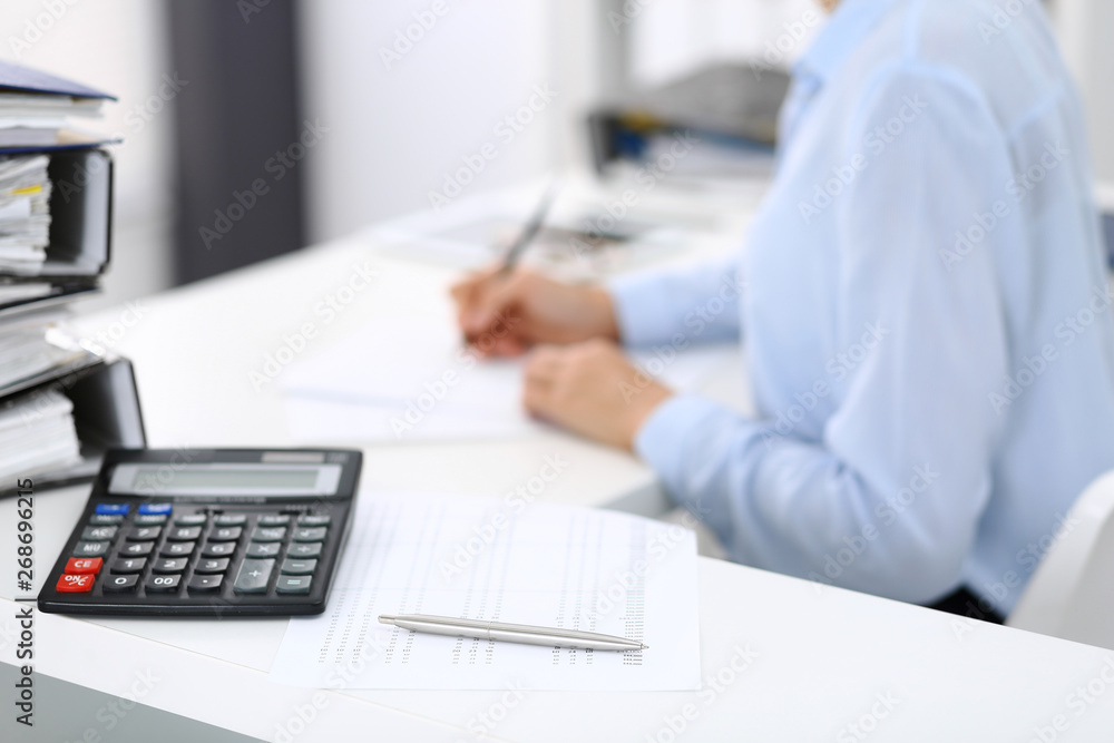 Calculator and binders with papers are waiting to be processed by business woman or bookkeeper back in blur. Internal Audit and tax concept Calculator and binders with papers are waiting to be processed by business woman or bookkeeper back in blur. Internal Audit and tax concept