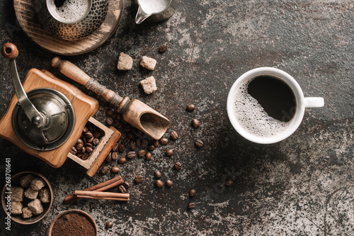 Coffee cup with coffee grinder and coffee beans on dark textured background.