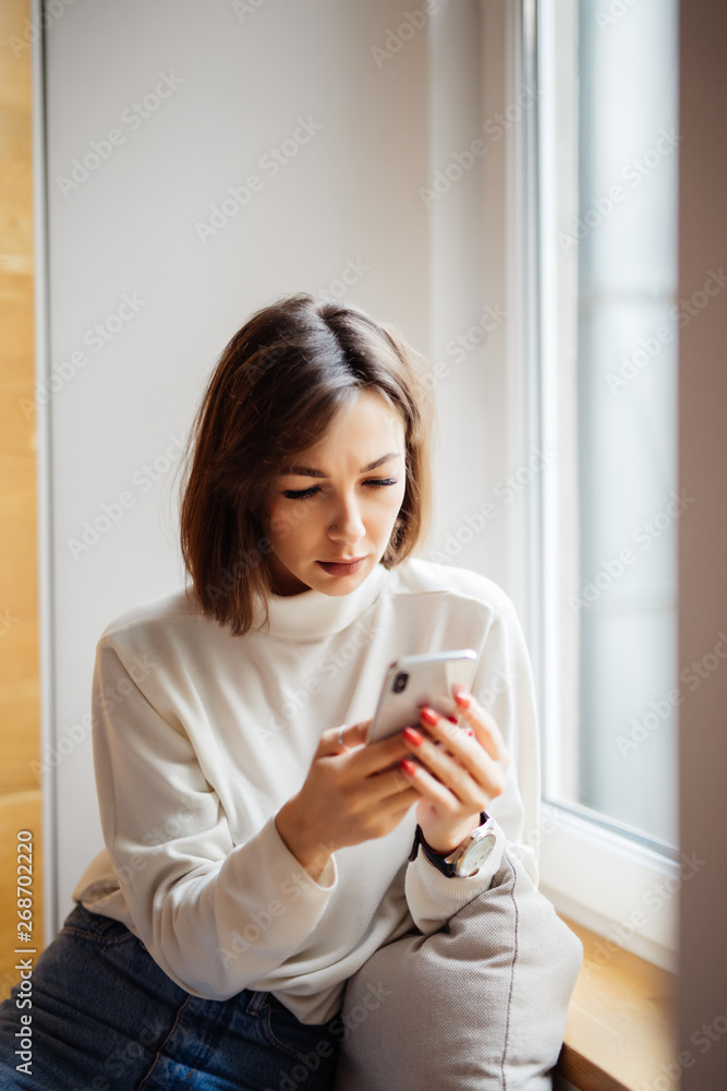 Young pretty woman typing on mobile phone on windowsill Young pretty woman typing on mobile phone on windowsill
