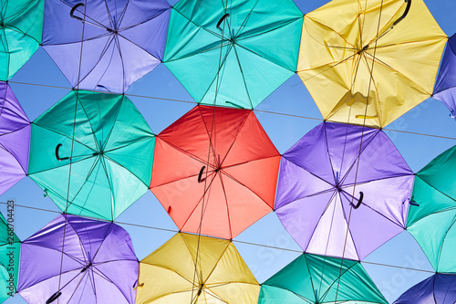 Background of multicolored umbrellas hanging against the blue sky.