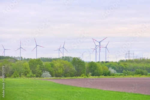 Wind mill turbines in field with blue sky and clouds and green summer grass on the front. Alternative renewable energies. Ecological clean energy. Electricity wind stations. Wind turbine generator 