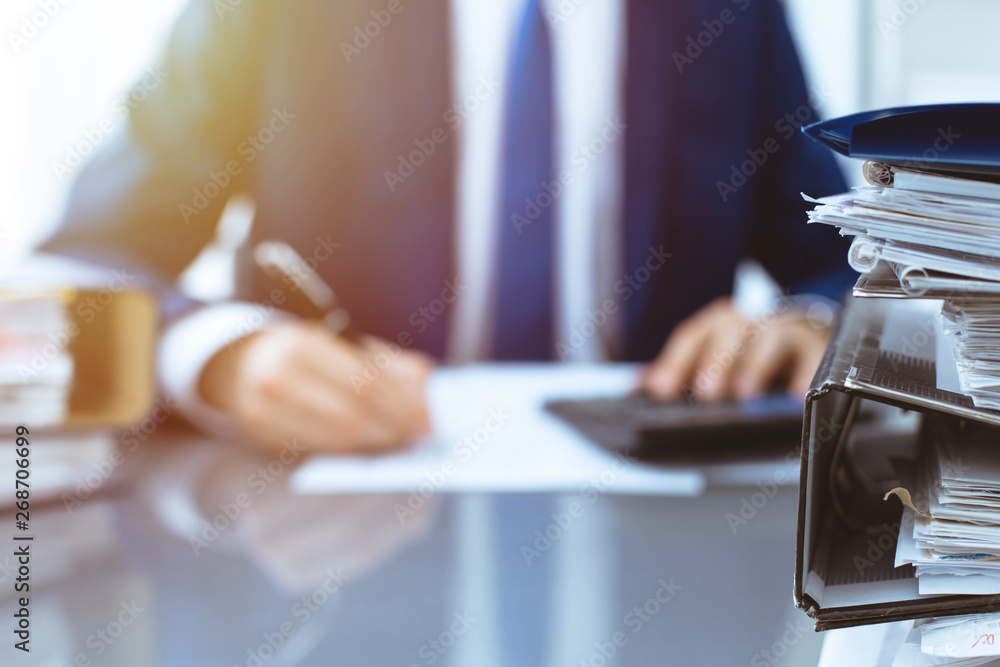 Binders with papers waiting to be processed with businessman or bookkeeper back in blur. Accounting planning budget. Audit, insurance and business concept Binders with papers waiting to be processed with businessman or bookkeeper back in blur. Accounting planning budget. Audit, insurance and business concept