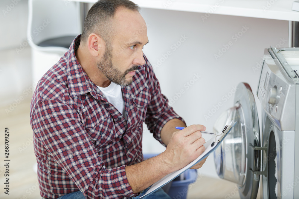 mature serviceman inspecting washing machine