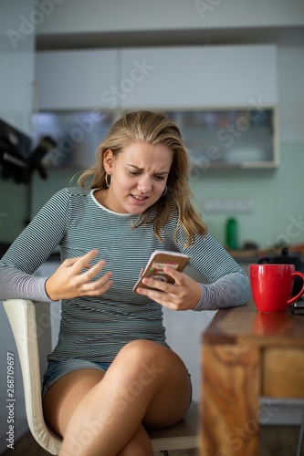 Teenage girl using her cell phone, being angry, while having a cup of tea in modern kitchen setting (shalllow DOF, color toned image) photo