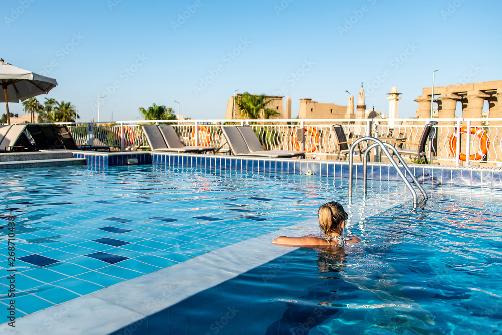 Young beautiful Woman sunbathing in swimming pool at luxurious looking on sunshade parasol in Egypt Luxor