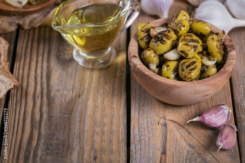 Grilled olives with garlic, olive oil and spices on wooden background