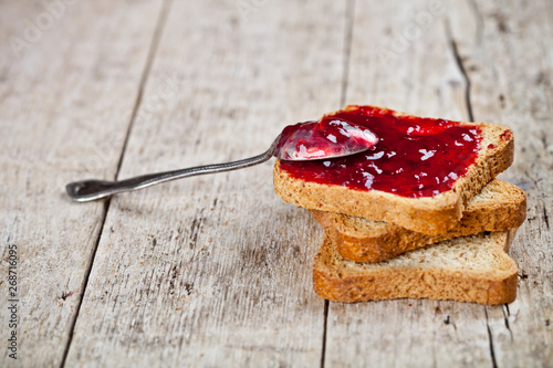 Toasted cereal bread slices with homemade cherry jam and spoon closeup on rustic wooden table background.