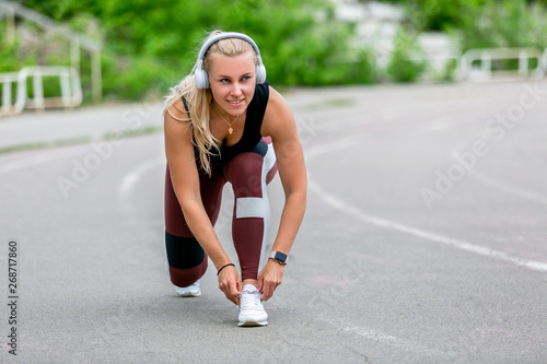 Fitness lifestyle. Young woman in headphones tying the laces before jogging. Workout at the stadium. Healthy life concept