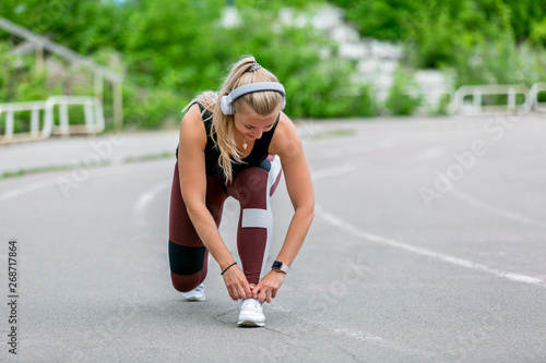 Fitness lifestyle. Young woman in headphones tying the laces before jogging. Workout at the stadium. Healthy life concept
