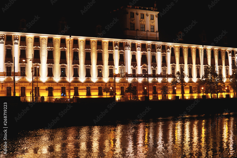 Large old house, lit at night. City of Wroclaw. Reflection in water