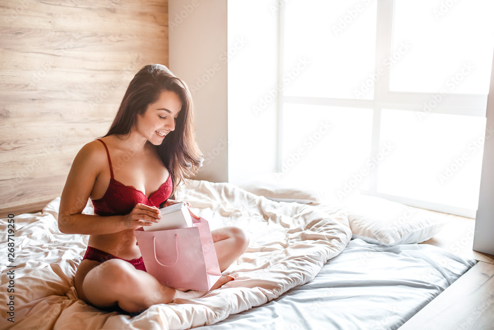 Seductive young naked dark-haired woman on bed in morning. Happy positive  sexy model sit with legs crossed and look inside bag. Alone in room. Hot  brunette. Stock Photo | Adobe Stock