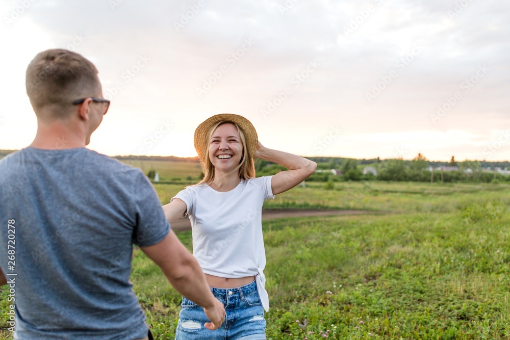 Girl in a straw hat walking with a guy on the field on a summer day outdoors