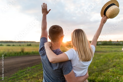 Young married couple at sunset on a summer day. Say goodbye to the sun waving his hands