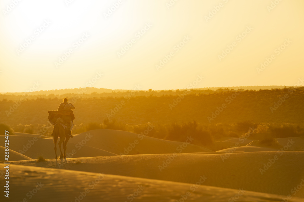 Stunning view of a man riding a camel on the dunes of the Thar Desert in Rajasthan during sunset. India. The Thar Desert is a large arid region in the northwestern part of the Indian subcontinent. Stunning view of a man riding a camel on the dunes of the Thar Desert in Rajasthan during sunset. India. The Thar Desert is a large arid region in the northwestern part of the Indian subcontinent.