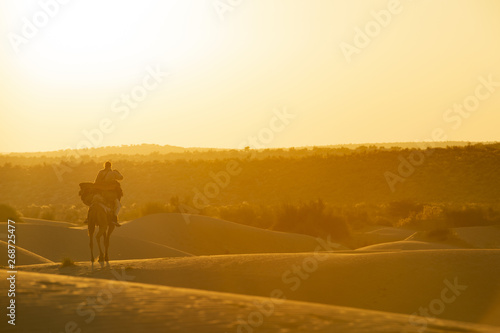 Stunning view of a man riding a camel on the dunes of the Thar Desert in Rajasthan during sunset. India. The Thar Desert is a large arid region in the northwestern part of the Indian subcontinent.