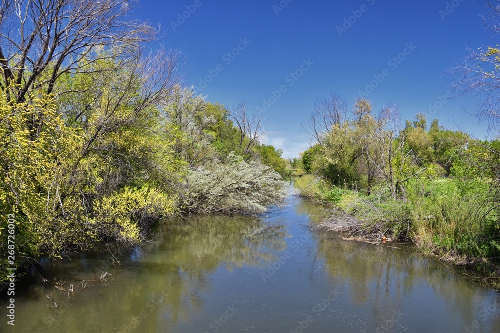 Jordan River Parkway Trail, Redwood Trailhead bordering the Legacy Parkway Trail, panorama views with surrounding trees and silt filled muddy water along the Rocky Mountains, Salt Lake City, Utah. 