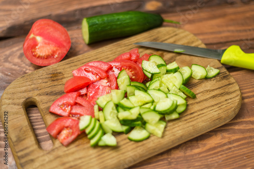Sliced fresh tomato and cucumber on a wooden board. Cooking vegetable salad. The concept of healthy, vegan food.