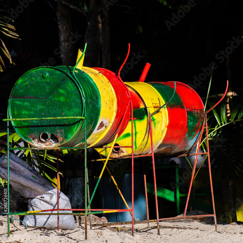 Jamaican jerk pan/ grill in Rasta colors in Jamaica. Used to cook jerk fish, chicken, pork meals outdoors. It is a metal drum cut down the middle, placed sideways on metal stand, filled with coal.