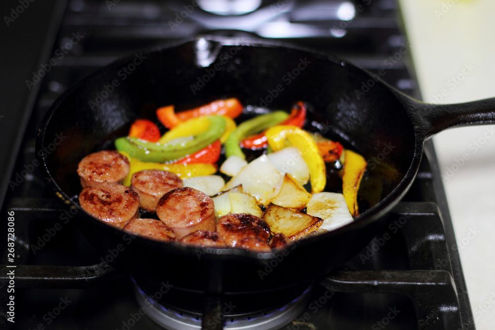 Sausage cooking on the stove in a cast iron skillet with bell peppers and onion. Sausage cooking on the stove in a cast iron skillet with bell peppers and onion.