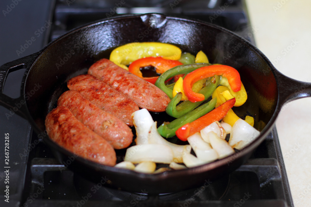 Sausage cooking on the stove in a cast iron skillet with bell peppers and onion. Sausage cooking on the stove in a cast iron skillet with bell peppers and onion.