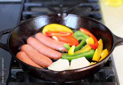 Sausage cooking on the stove in a cast iron skillet with bell peppers and onion.