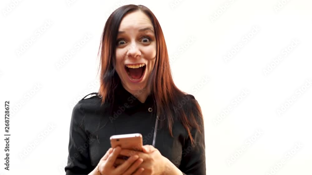 Cheerful woman holding a mobile phone and looking at it with a smile standing on a white background