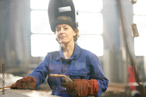Tableau sur toile Waist up portrait of smiling female welder posing confidently while working at i
