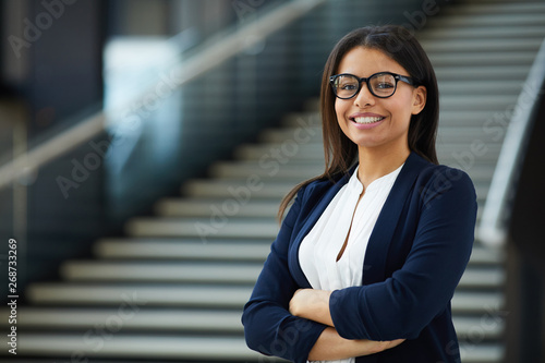 Smiling smart attractive young black lady in glasses standing in lobby and looking at camera, she working in prosperous company photo