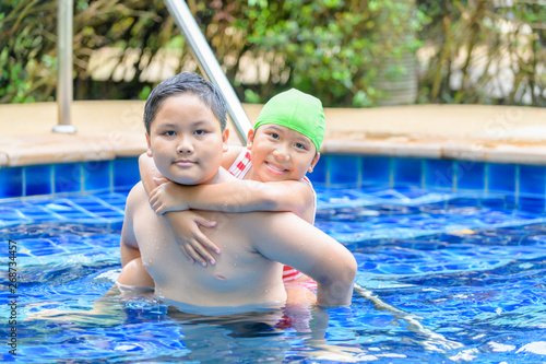 brother holding sister on his back in swimming pool