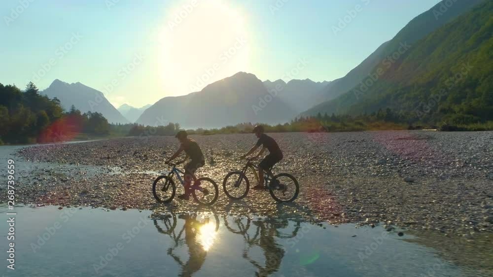 DRONE, LENS FLARE, SILHOUETTE: Golden sun rays shine on two travelers ...