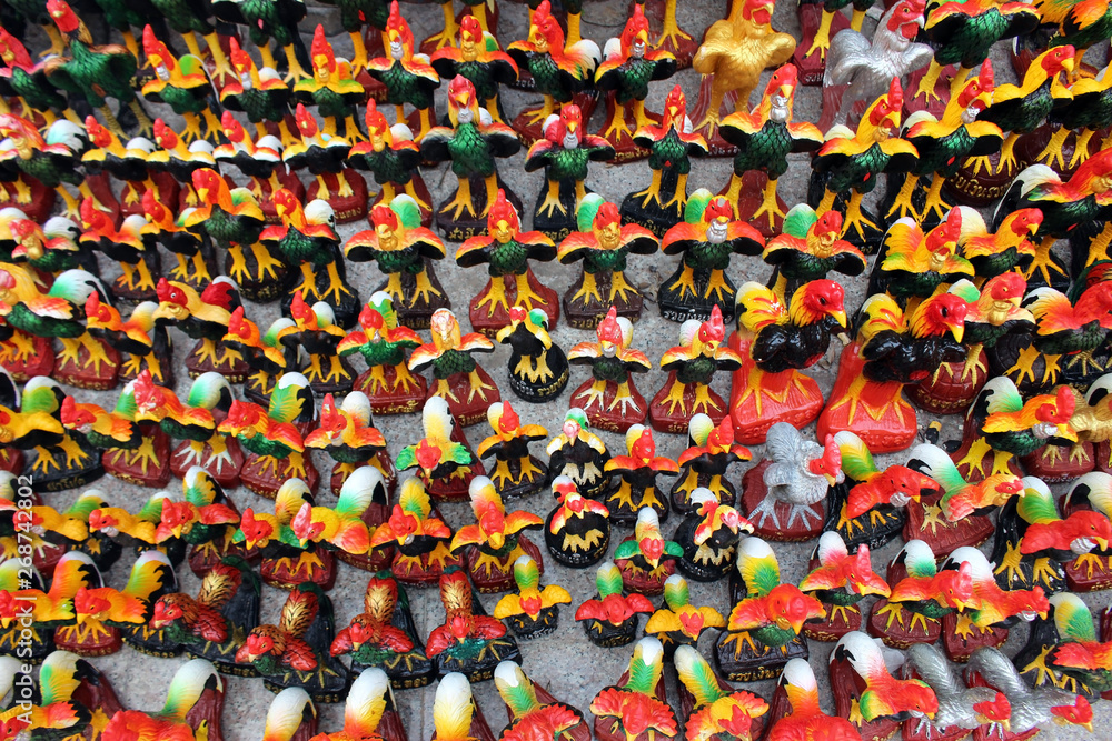Large collection of Rooster statues in rows at a Buddhist temple forms a bright pattern - above view.