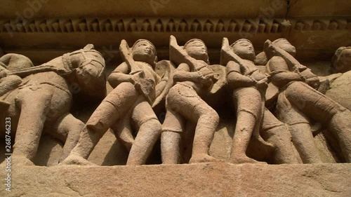 A hand held, low angle, close up shot of some stone sculptures of ancient people going to battle. photo