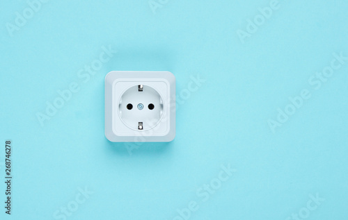 White plastic power socket on blue background. Wall with copy space. Minimalism