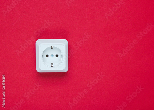 White plastic power socket on red background. Wall with copy space. Minimalism